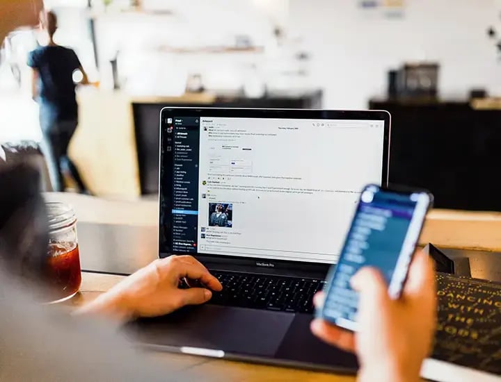 Foto einer Person von Hinten am Laptop die Smartphone ind er Hand hält