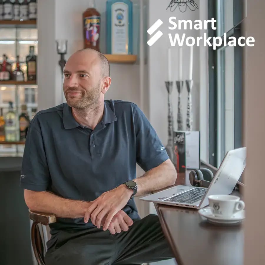 Person sitzt mit ihrem digitalen Arbeitsplatz Laptop in einem Café, SmartIT Logo in der Ecke