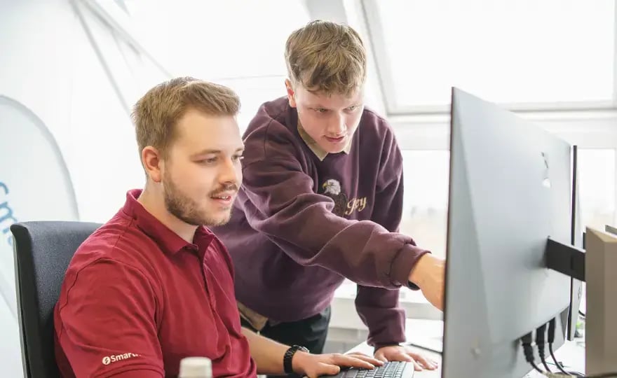 Stehender Mitarbeiter von SmartIT zeigt sitzendem Mitarbeiter etwas auf dessen Monitor