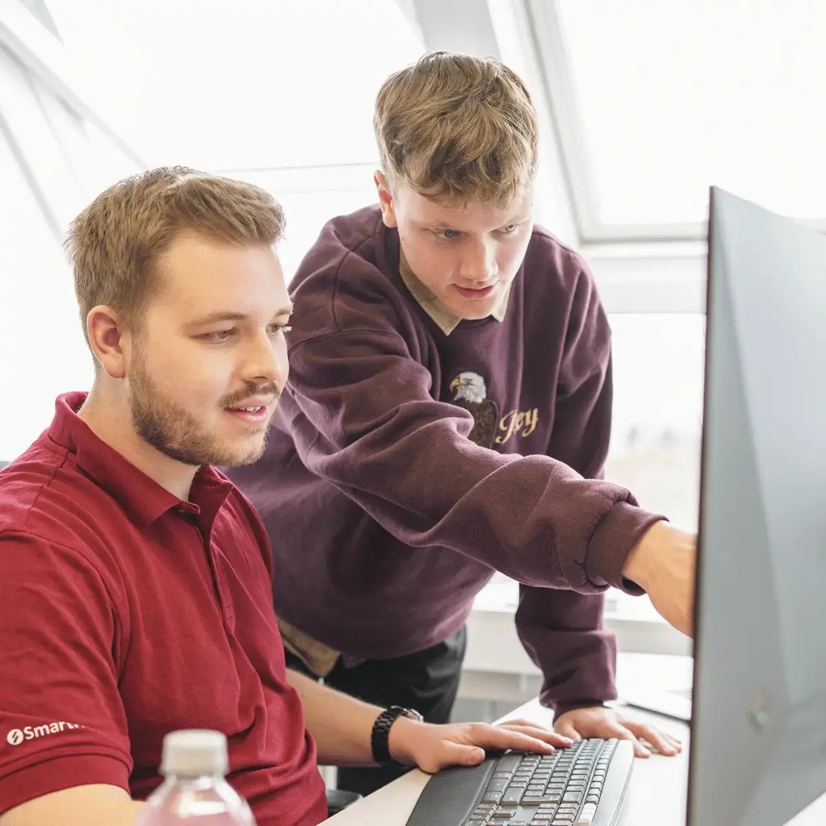 Stehender Mitarbeiter von SmartIT zeigt sitzendem Mitarbeiter etwas auf dessen Monitor